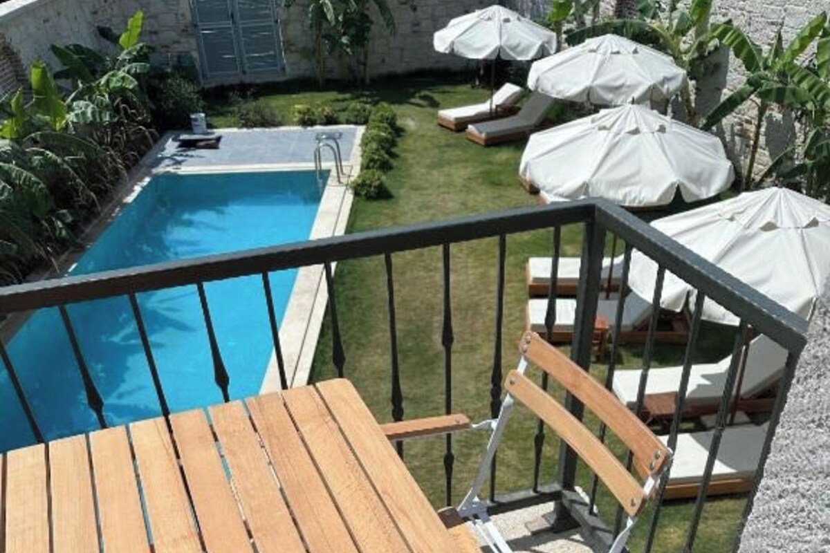 A wooden table and chair set on a balcony with a pool in the background.