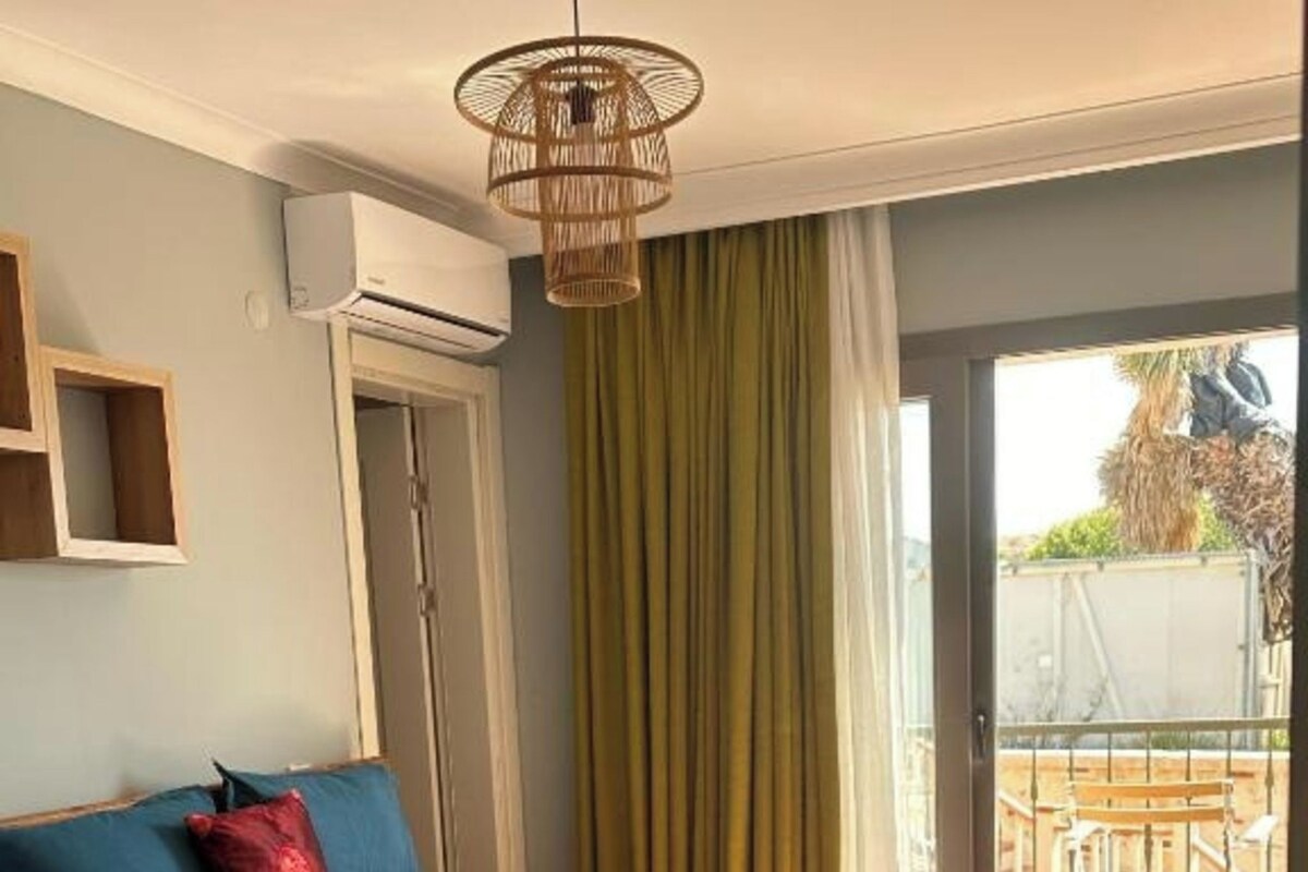 A bedroom with a bed, a wooden floor, a ceiling fan, and a view of the outside.