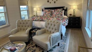 Un dormitorio con una cama grande, dos sillones, una mesita de noche y un ventanal con persianas.