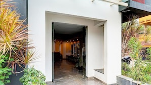 A modern building entrance with a glass door, a tiled floor, and potted plants on either side.