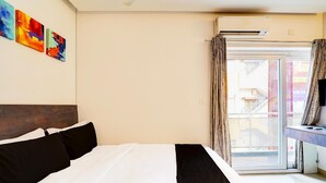 A hotel room with a bed, a desk with a computer, and a window with curtains.