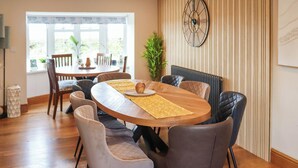 A dining area with a round wooden table, six chairs, and a large wall clock. - 6 bedroom accommodation in Narbeth (Narbeth)