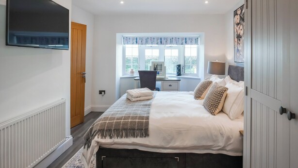 A bedroom with a bed, a desk, a chair, a TV, and a window with curtains. - 6 bedroom accommodation in Narbeth (Narbeth)