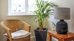 A wicker chair with a cushion, a potted plant, and a table with a lamp. - 6 bedroom accommodation in Narbeth (Narbeth)