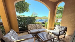 Un patio couvert avec un sol à carreaux, un canapé, deux fauteuils et une table en bois.