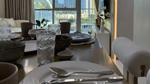 Un coin repas avec une table dressée pour deux personnes, une vue sur le paysage urbain grâce à de grandes fenêtres et un aménagement intérieur moderne.