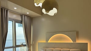 Une chambre moderne dotée d’un grand lit, offrant une vue sur la mer et agrémentée d’un luminaire au plafond au design unique.