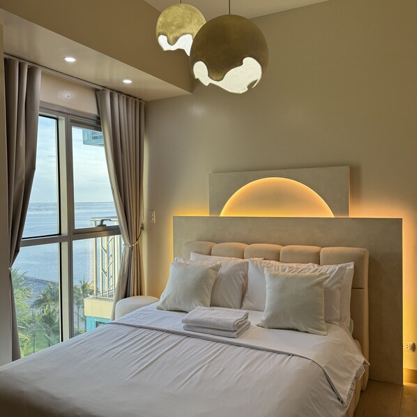 A modern bedroom with a large bed, a view of the sea, and a unique ceiling light fixture. - Panoramic Landscape and Seaview, 2BR, Near Airport, Beside the Bay - 25 (Paranaque)