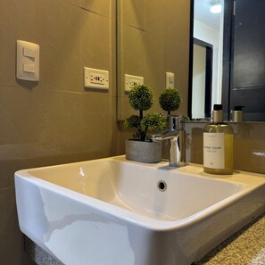 A bathroom with a white sink, a mirror, a potted plant, and a bottle of hand soap. - Panoramic Landscape and Seaview, 2BR, Near Airport, Beside the Bay - 25 (Paranaque)