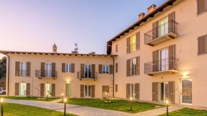 A multi-story building with balconies, a paved courtyard, and a small tower. - Katia House - Lavender Apartment (Castelnuovo Calcea)