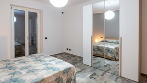 A bedroom with a bed, a wardrobe, a mirror, and a ceiling light. - Katia House - Lavender Apartment (Castelnuovo Calcea)