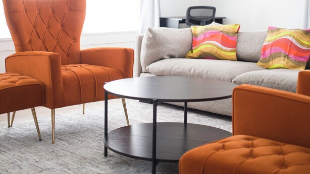 A modern living room with a sofa, two armchairs, a coffee table, and a ceiling fan.