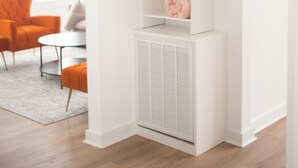 A modern room with a white built-in shelving unit, a radiator, and a seating area with an orange chair and a small table.