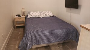 A bedroom with a bed, a nightstand, a lamp, a TV, and a painting on the wall.