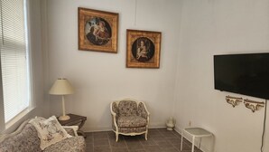 A living room with a floral sofa, a patterned armchair, a small side table with a lamp, and two framed pictures on the wall.