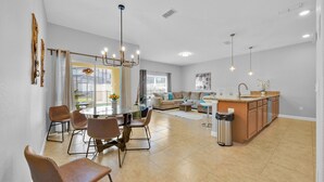 Amplia sala de estar con una mesa y sillas de comedor, una cocina con una isla grande, y vistas al exterior.