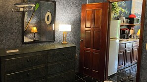 A bathroom with a dark marble vanity, a framed sign reading "GONE FISHING," a mirror, a wall-mounted lamp, and a wooden door leading to a kitchen area.