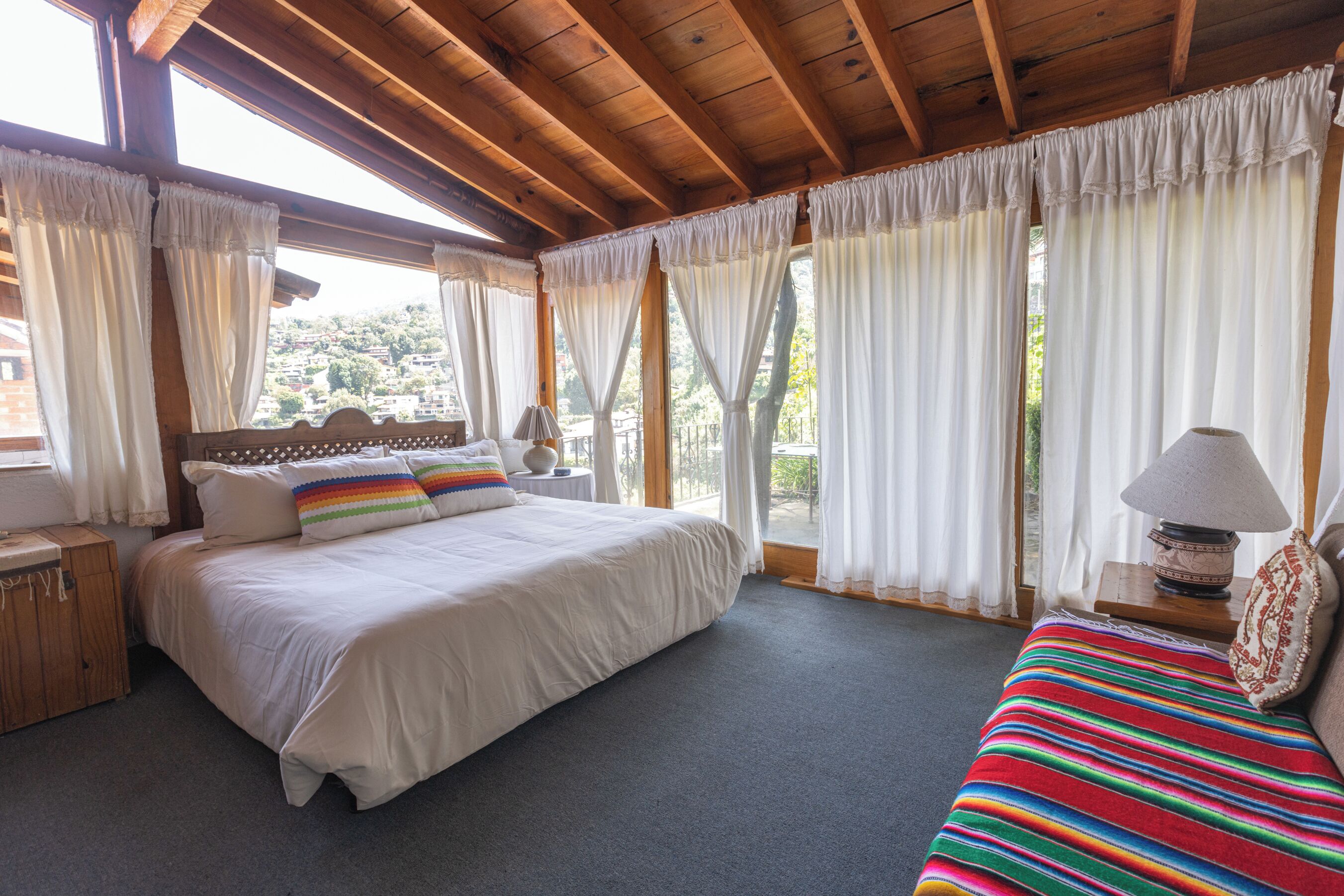 Ein Schlafzimmer mit einem großen Bett, einem Einzelbett, einem Holz-Kopfstück, einem Nachttisch, einer Lampe und Blick ins Freie.