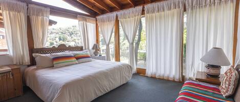 Ein Schlafzimmer mit einem großen Bett, einem Einzelbett, einem Holz-Kopfstück, einem Nachttisch, einer Lampe und Blick ins Freie.