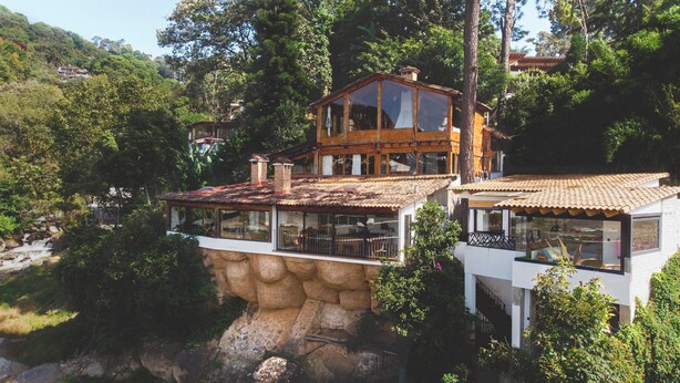 Une maison construite sur une falaise, avec un chalet en bois et un bâtiment blanc doté de grandes fenêtres.