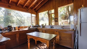 Une cuisine rustique aménagée dans une cabane en bois, avec une grande table, des placards en bois et un réfrigérateur.