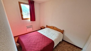 A small, single-bed room with a wooden headboard, a window with red curtains, and a wooden floor. - 100m from ski slopes, 7th floor, balcony, tv, ski locker, 37m², Valfréjus (Valfréjus)
