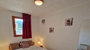 Quarto com cama de madeira, janela com cortina vermelha, quadros pendurados na parede, luz de teto e ar condicionado fixado na parede.