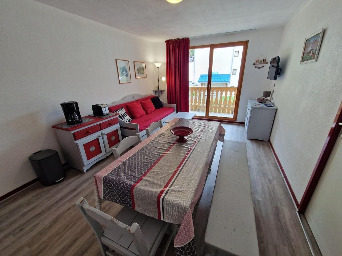 A room with a sofa, a dining table, a small kitchen area, and a sliding glass door leading to an outdoor balcony.