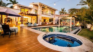A luxurious poolside area with a wooden deck, a hot tub, and a dining area with outdoor seating.