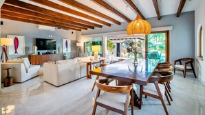 A spacious living area with a large wooden dining table, white sofas, and a TV.