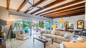 A spacious living area with a wooden ceiling, large windows, a sofa set, and a dining area.