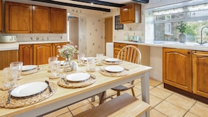 Uma cozinha moderna com armários de madeira, uma mesa de jantar posta para quatro pessoas e vista para o exterior pela janela.