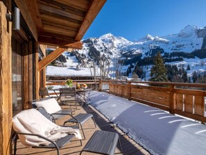A wooden deck with outdoor seating, a view of snow-covered mountains, and a clear sky.