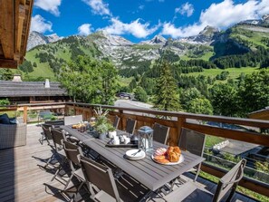 A wooden deck with a table set for breakfast, overlooking a mountainous landscape.