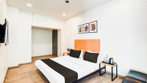 Ein modernes Hotelzimmer mit einem großen Bett, einem Holz-Kopfteil, einem kleinen Tisch mit Wasserkocher und einer Bank.