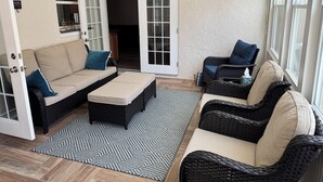 A cozy patio area with a beige sofa, a matching ottoman, and wicker chairs.