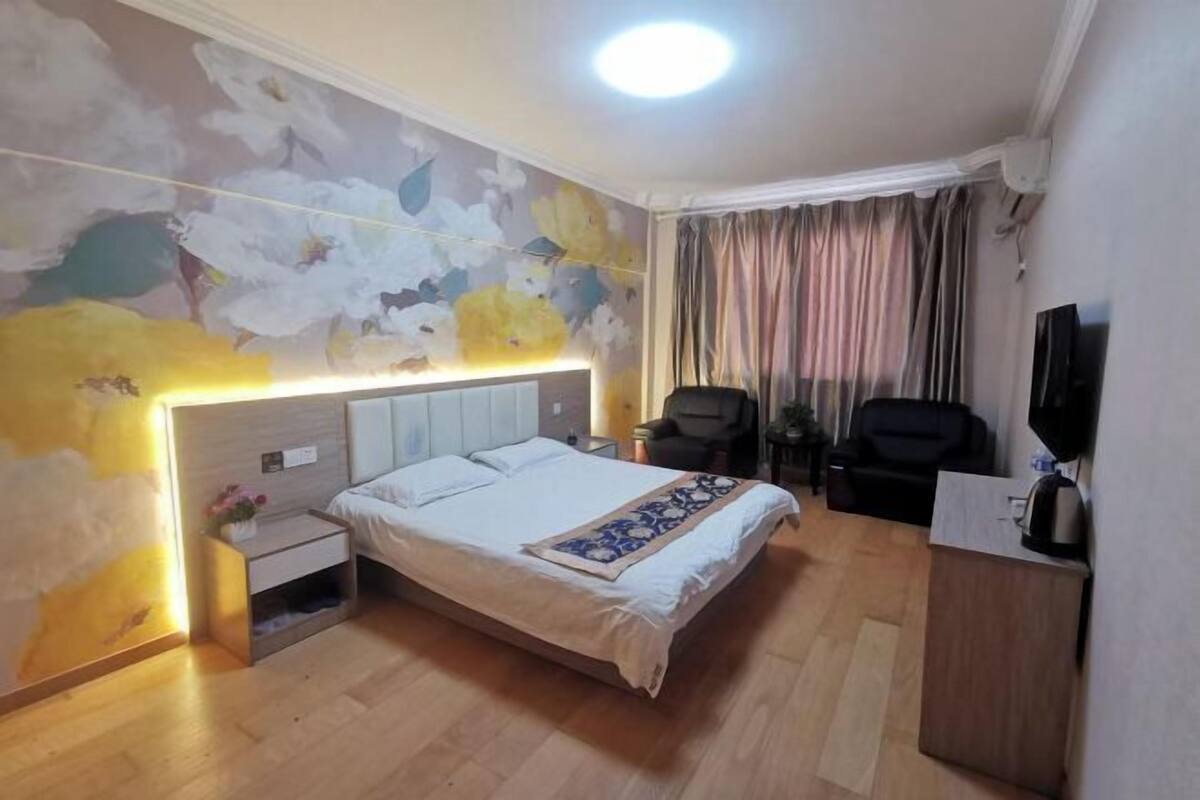 A hotel room with a bed, bedside table, nightstand, chair, desk, TV, and a floral wall mural.