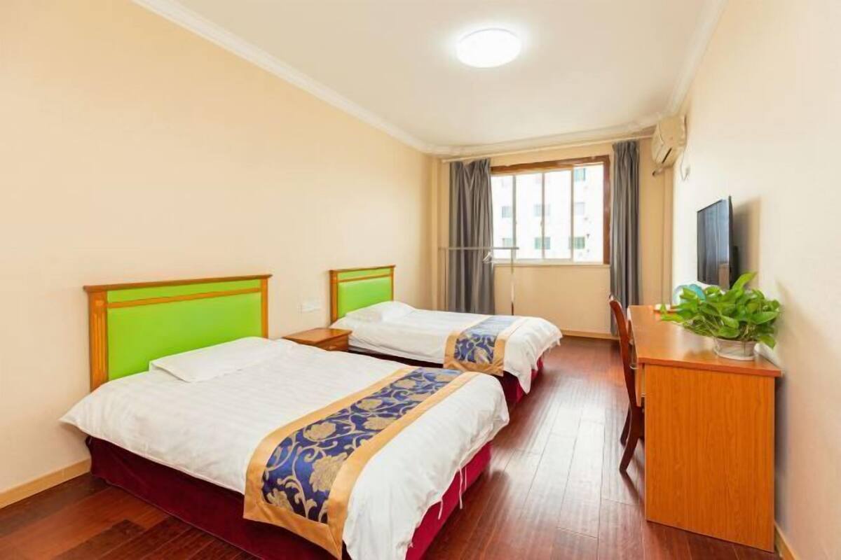 A hotel room with two beds, a desk, a television, and a window with curtains.