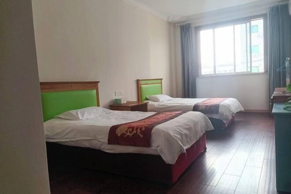 A hotel room with two beds, a window with curtains, a desk, and a chair.