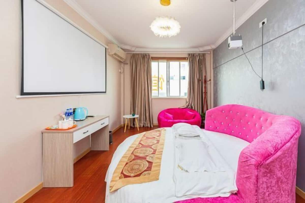 A hotel room with a bed, a desk, a chair, a projector, and a window.