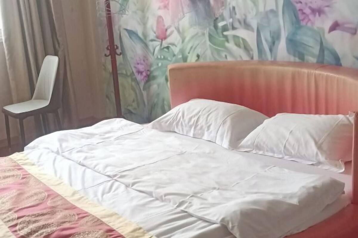 A bed with white bedding, a chair, and a floral wallpaper.