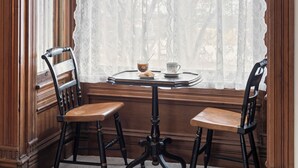 A corner room with a bay window, two wooden chairs, a small round table, and a white lace curtain. - Historic 1890, 3-bed Victorian townhome in welcoming Monett with WiFi, AC (Monett)
