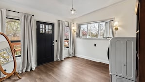 A spacious room with a wooden floor, a black door, and a window with curtains. - Historic 1890, 3-bed Victorian townhome in welcoming Monett with WiFi, AC (Monett)
