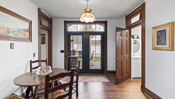 A dining area with a wooden table and chairs, a chandelier, and a view through a glass door to the outside. - Historic 1890, 3-bed Victorian townhome in welcoming Monett with WiFi, AC (Monett)
