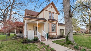 A two-story house with a front porch, a covered entryway, and a small front yard. - Historic 1890, 3-bed Victorian townhome in welcoming Monett with WiFi, AC (Monett)