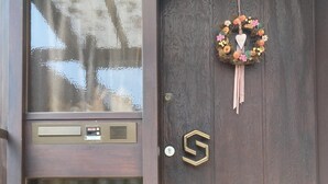 Un perro frente a una puerta de madera oscura con un adorno festivo y una cerradura.