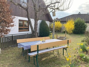 Un banco de madera con mantel a cuadros en un jardín con flores amarillas y un árbol.