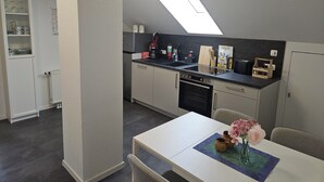 Una cocina compacta con tragaluz, una mesa de comedor con un jarrón de flores y un armario blanco con vajilla.