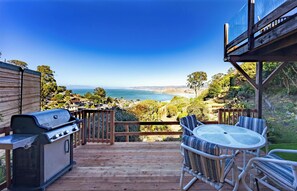 A wooden deck with a grill, a round table with chairs, and a view of the ocean and hills. - Small Home with Ocean View walk to Restaurants, Brewery, Shops, Beach (Pacifica)