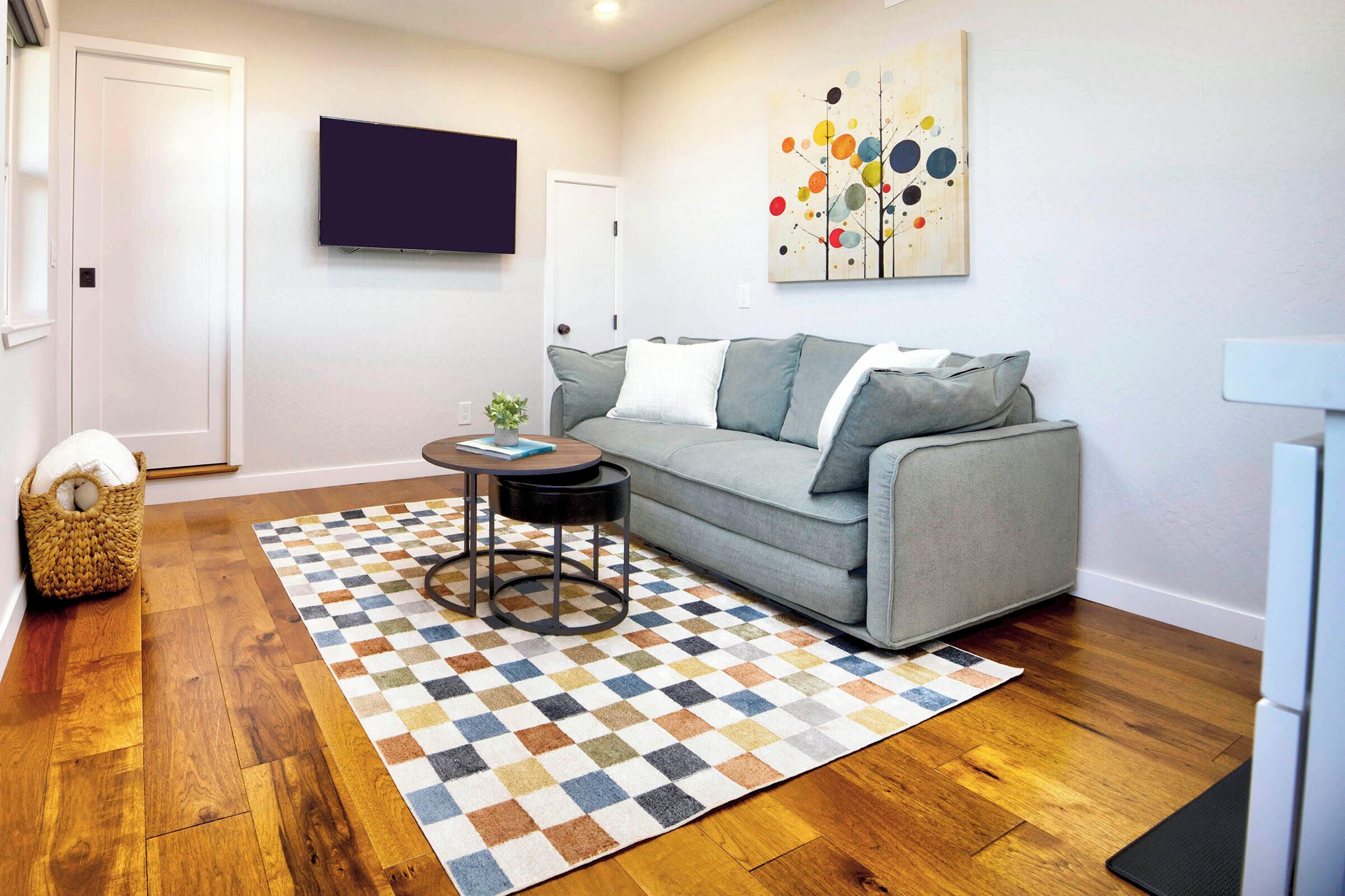A living room with a grey sofa, a patterned rug, a small round table, and a wall-mounted TV.